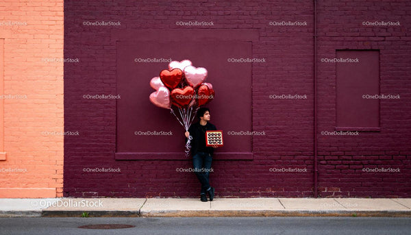 Man holding heart balloons and chocolates on street
