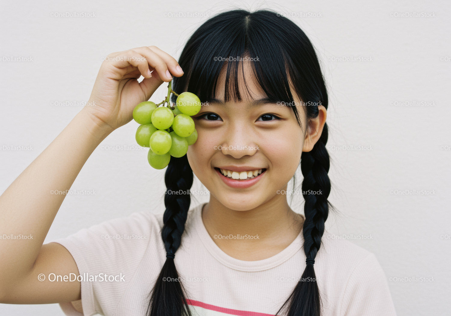 Smiling Girl with Braids Holding Fresh Green Grapes