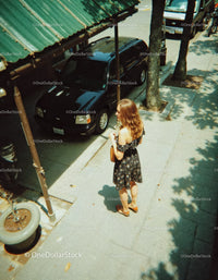 Woman in Floral Dress Standing on Sidewalk Near Parked Car in City