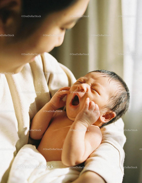 Newborn baby yawning in mother’s gentle embrace