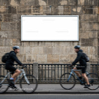 Two Cyclists Passing by Blank Urban Billboard on Stone Wall