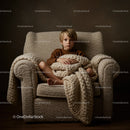 Thoughtful boy sitting wrapped in chunky knit blanket