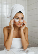 Young woman applying under eye patches in modern bathroom
