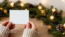 Hands Holding Blank Card Near Festive Pine Garland JPG Mockup Image preview