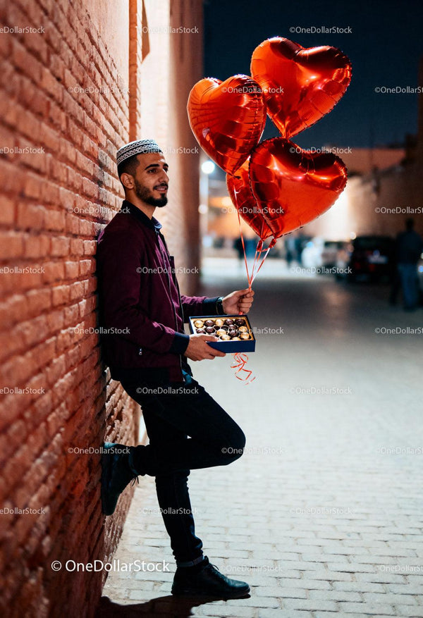 Young man with heart balloons and chocolates at night
