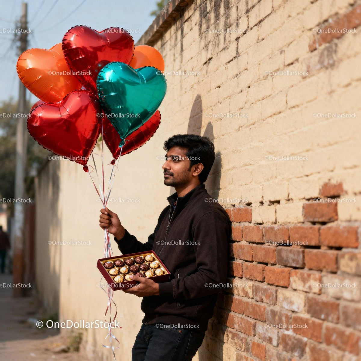 Man holding heart balloons and chocolates by brick wall