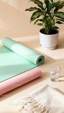 Rolled pastel yoga mats next to green houseplant and water