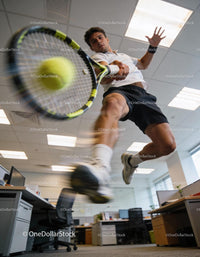 Athlete hitting tennis ball with racket in office space