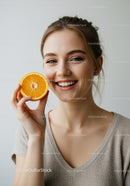 Young Woman Smiling with Orange Half in Bright Studio