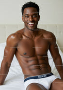 Smiling athletic man sitting on white bed in underwear