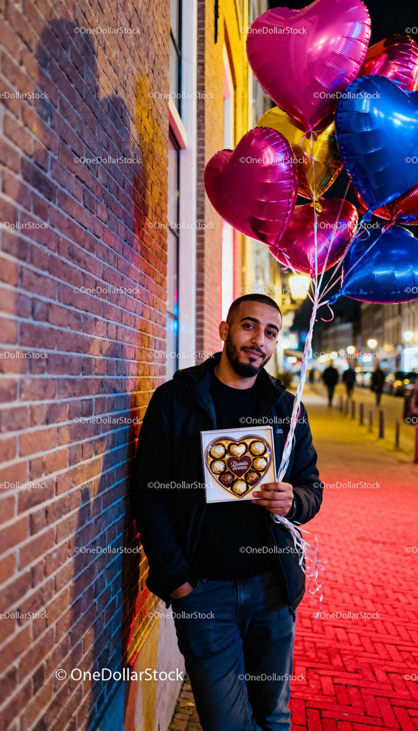 Man Holding Heart-Shaped Chocolates and Balloons Outdoors