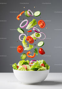 Fresh vibrant vegetables falling into white salad bowl
