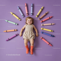 Happy toddler lying among oversized colorful crayons