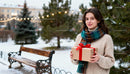 Young woman with gift in snowy park with festive lights