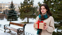 Young woman with gift in snowy park with festive lights
