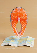 Fresh salmon steak above folded world map on tan background
