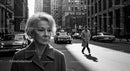 Elderly Woman in Busy City Street Surrounded by Vintage Cars