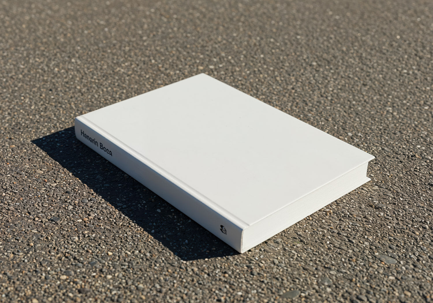 Blank white hardcover book lying on textured asphalt