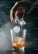 Hand Adding Ice Cubes to Whisky Glass with Splash