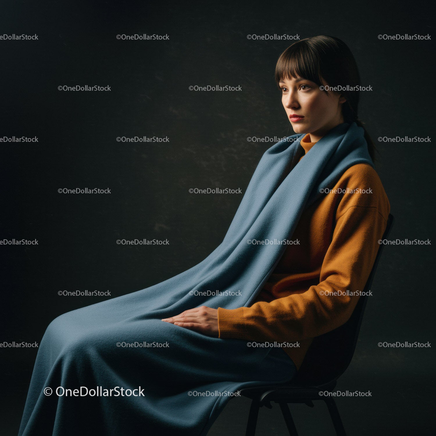 Elegancka kobieta siedząca w ciemnym studiu z niebieskim szalikiem i brązowym swetrem