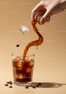 Hand pouring iced coffee with floating ice cube and beans