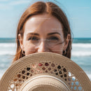 Happy Woman with Wind-Blown Hair Holding Straw Hat at Beach