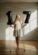 Blonde woman holding black balloon numbers 17 indoors