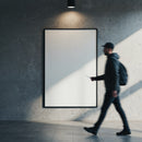 Man walking past blank illuminated poster on concrete wall