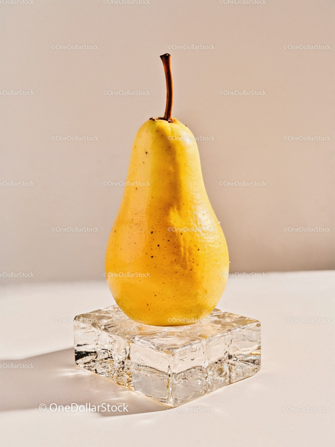 Fresh yellow pear on clear ice cube with beige background