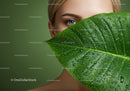 Close-up of Woman with Blue Eye Behind Green Tropical Leaf with Water Droplets