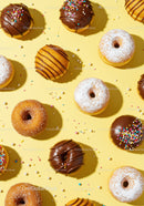 Assorted colorful donuts with sprinkles on yellow background