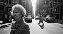 Elderly Woman in Busy City Street Surrounded by Vintage Cars