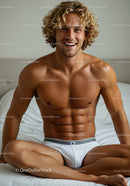 Smiling muscular man in white briefs sitting on bed