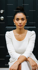 Elegant woman in white dress sitting against dark door