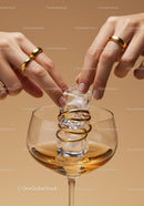 Fingers placing ice cubes in glass with golden rings