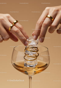 Fingers placing ice cubes in glass with golden rings
