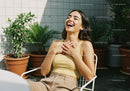 Joyful Woman Sitting Outdoors Surrounded by Green Potted Plants