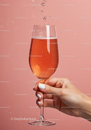 Hand Holding Sparkling Rosé Wine Glass Against Pink Background