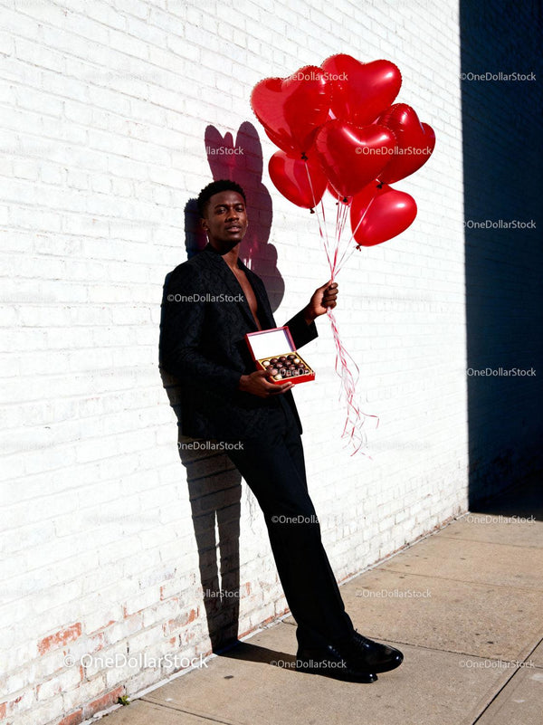 Stylish man holding heart balloons and chocolates gift