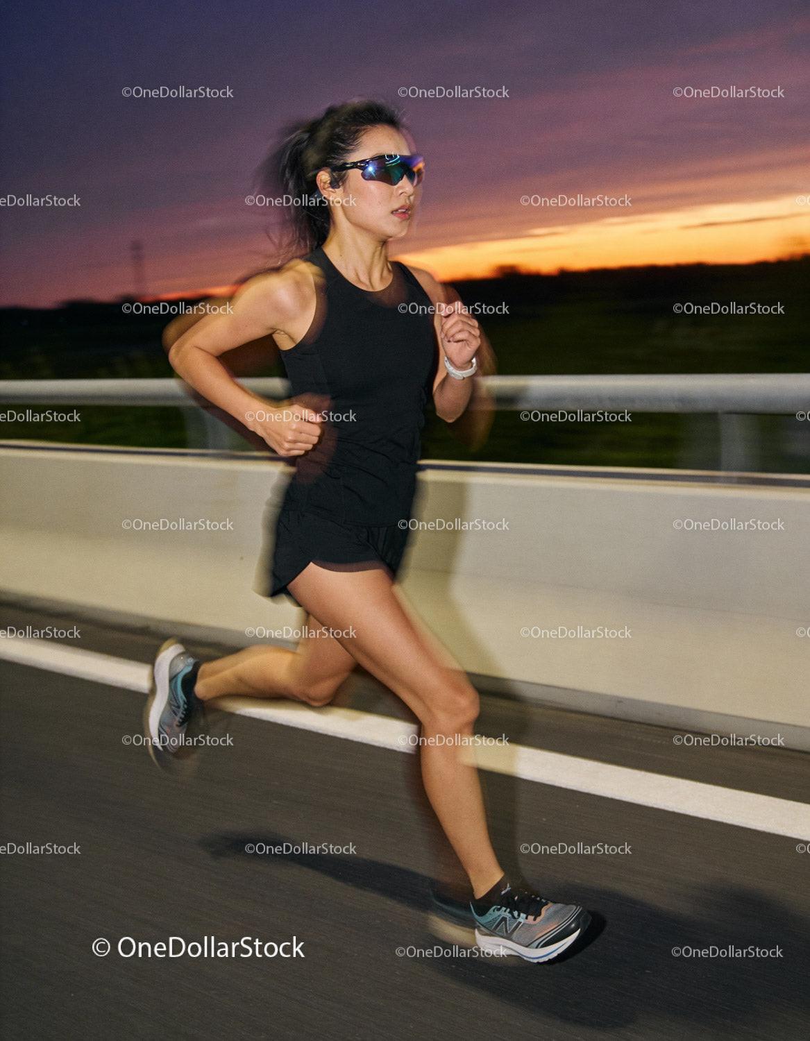 Athletic woman running on road at sunset