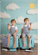 Two boys playing with paper planes on suitcases indoors
