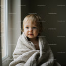 Toddler wrapped in cozy blanket by the window