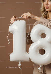 Woman Holding White Number 18 Balloons Against Brown Background