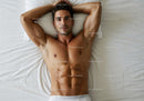 Relaxed young man lying shirtless on white bed