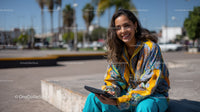 Young Woman Smiling Sitting Outdoors with Tablet in City Street