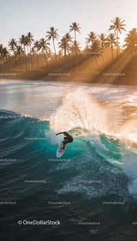 Surfer Riding Wave at Sunset Near Palm Trees