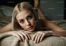 Portrait of a Young Woman with Blonde Hair and Bright Blue Eyes Relaxing on a Bed