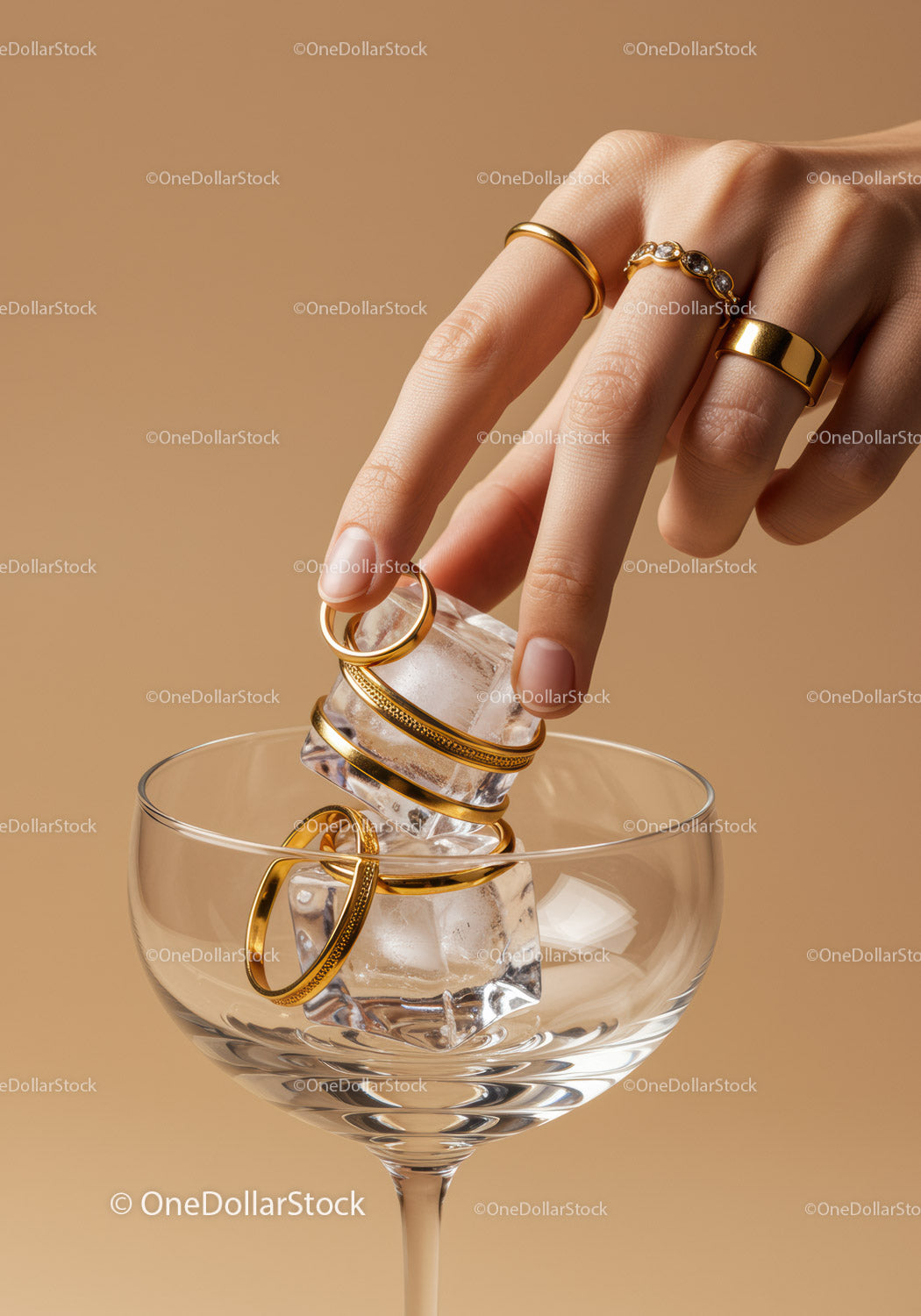 Hand placing golden rings on ice cubes in glass