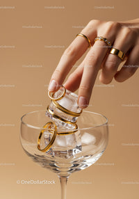 Hand placing golden rings on ice cubes in glass