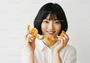 Young Woman Holding Fresh Tangerine and Orange Peel in Bright Studio